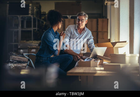 Deux partenaires travaillant ensemble à l'entrepôt pour vendeur en ligne d'affaires. Les gens à discuter lors de la préparation de l'emballage à la livraison. Banque D'Images