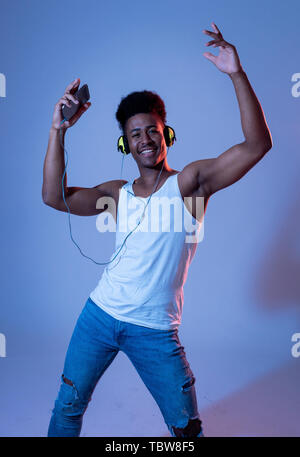 Strong african american man jeune danseur à l'écoute de la musique en ligne danser et chanter avec le casque. Portrait artistique de danse disco avec neon Banque D'Images