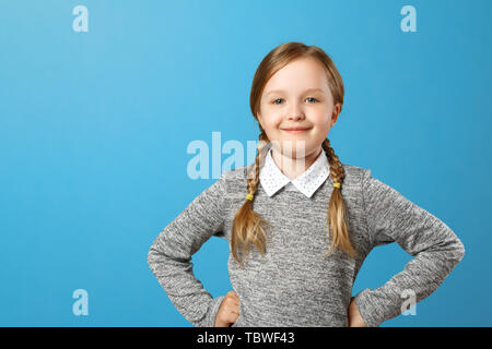 Portrait of a cute little girl sur un fond bleu. La lycéenne fait mains sur le côté et regarde dans la caméra. Copier l'espace. Banque D'Images