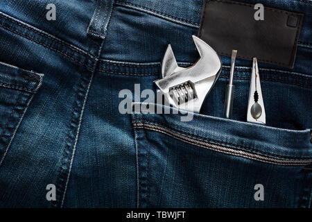 Clé à molette, une pince et un tournevis dans la poche arrière d'un jean bleu. Vue en gros plan. Banque D'Images