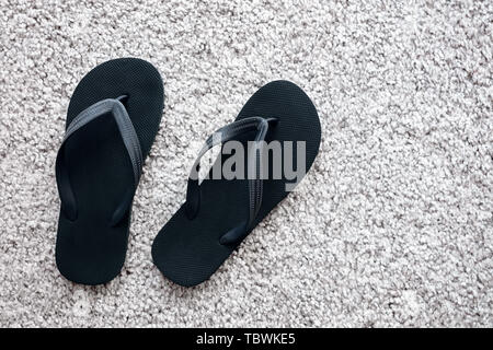 Paire de tongs en caoutchouc noir sur tapis blanc. Mise à plat. Banque D'Images