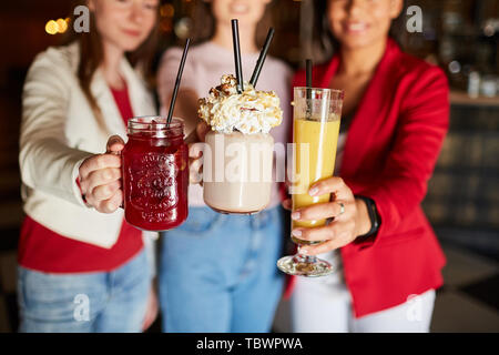 Close-up de jeunes femmes qui atteignent les mains avec des cocktails rafraîchissants pour partie à l'appareil photo tout en ayant du plaisir ensemble Banque D'Images