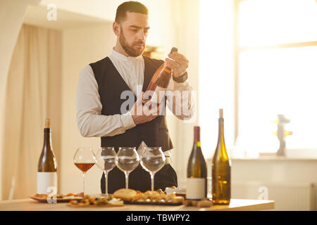 Taille portrait de sommelier professionnel tenant une bouteille de rose lors de la préparation pour une séance de dégustation de vin dans la lumière du soleil, copy space Banque D'Images