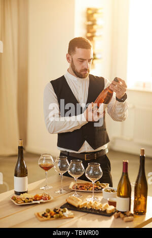 Taille portrait de sommelier professionnel tenant une bouteille de rose lors de la préparation pour une séance de dégustation de vin dans la lumière du soleil Banque D'Images