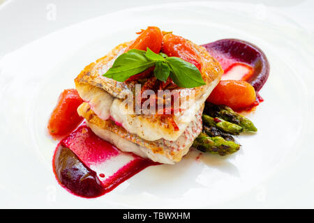 Close up d'un vivaneau rouge grillé poêlé filet de poisson aux asperges, betterave, sauce tomates de San Marzano de cerises et basilic sur une plaque blanche natural Banque D'Images