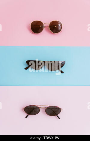 Trois lunettes sur un fond rose et bleu pastel. Le concept de l'été et de vacances élégant. Photo verticale. Banque D'Images