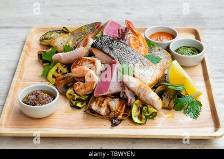 Close up of a mixed fruits de mer grillés et plateau de poisson sur une planche en bois, saumon, thon, calamars, crevettes, pétoncles, palourdes, moules, légumes, citron,, spi Banque D'Images