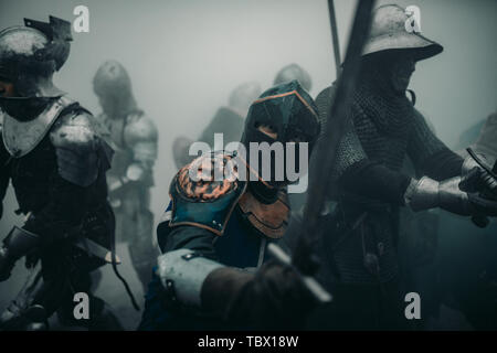 L'Escouade de combat de chevaliers médiévaux des croisés sont dans les armures et casques pendant la bataille avec des épées dans matin brumeux. Banque D'Images