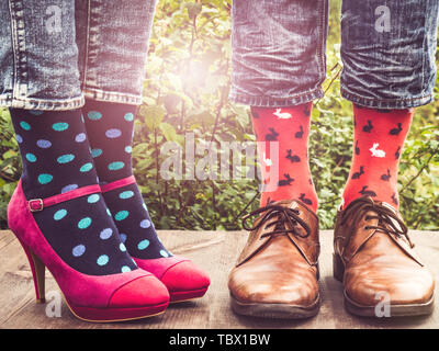 Les hommes et les femmes chaussures à la mode dans les jambes, lumineux, chaussettes multicolores sur une terrasse en bois sur l'arrière-plan d'arbres verts et des rayons de soleil. Close-up Banque D'Images