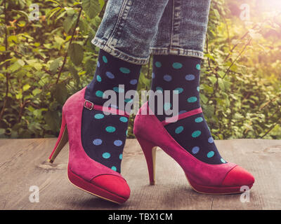 Les jambes des femmes dans le quartier branché de chaussures, lumineux, chaussettes multicolores sur une terrasse en bois sur l'arrière-plan d'arbres verts et des rayons de soleil. Close-up. Concept Banque D'Images