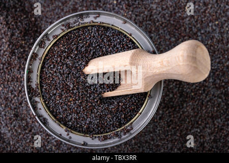 Un grain d'opium dans un peut sur une table de cuisine. Récupérer les graines de pavot et cuillère en bois sur une cuve de stockage. Fond sombre. Banque D'Images