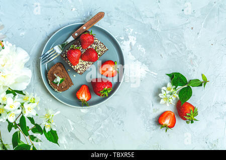 Rollcake chocolat avec fraises fraîches sur plaque en céramique, de jasmin et de pivoines blanches sur la surface de béton gris clair table. Haut de la vue, télévision lay, copie Banque D'Images