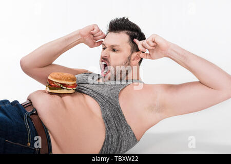 L'excès de l'homme criant avec burger sur ventre couché et faire l'exercice abs on white Banque D'Images