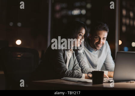 Smiling businesspeople sitting travailler overtme la nuit Banque D'Images