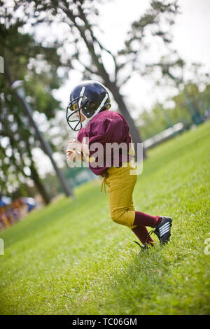 Jeune garçon portant un casque et uniforme de football américain sur une pelouse dans un parc. Banque D'Images