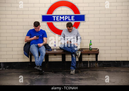 Deux hommes assis sur un banc sur la plate-forme à la station de métro Temple et regardez leurs téléphones mobiles. Chacune dispose d'une bouteille de verre Banque D'Images