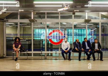 Un homme est assis seul sur un banc sur la plate-forme à la station de métro Westminster comme un groupe d'hommes asiatiques assis ensemble. Banque D'Images