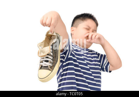 Dégoûté gros garçon tenant une paire de chaussures stinky malodorantes et isolé sur fond blanc, Banque D'Images