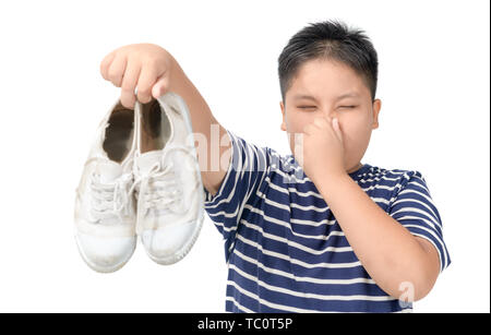 Dégoûté gros garçon tenant une paire de chaussures stinky malodorantes et isolé sur fond blanc, Banque D'Images