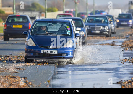 Les voitures qui circulent dans des flaques d'eau et de galets de plage sur une route côtière après de fortes pluies d'orage après l'orage dans le West Sussex, Angleterre, Royaume-Uni. Banque D'Images