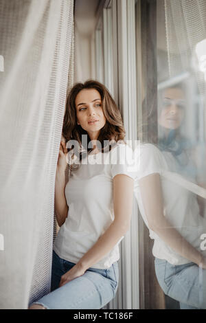 Jolie jeune femme en ouvrant les rideaux de la fenêtre d'appartements moderne après service Banque D'Images