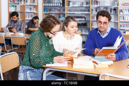 Les jeunes étudiantes concentré assis dans la bibliothèque de l'université, en collaboration avec le professeur Banque D'Images