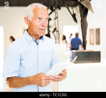 Senior male tourist brochure avec le programme de lecture de l'exposition au musée d'art Banque D'Images