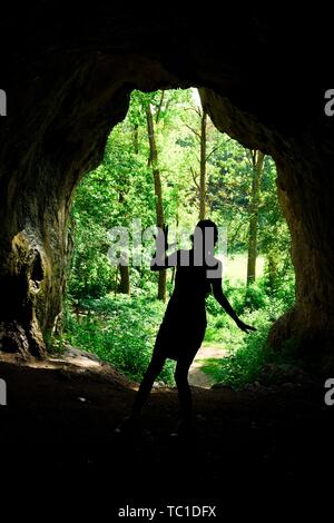 Silhouette de la jeune fille à l'entrée de grotte naturelle dans la forêt, jeune scout sur un voyage Banque D'Images