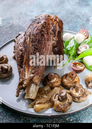 Close-up l'agneau rôti avec des champignons, épices et fines herbes sur une plaque ronde sur un fond en béton. La viande halal et de l'alimentation Banque D'Images