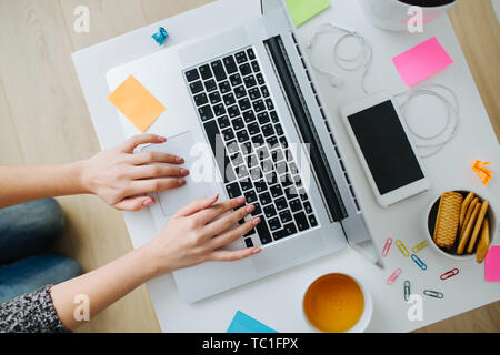 Espace de bureau à la maison des femmes. Femme mains tapant sur un ordinateur portable. Flatlay avec téléphone mobile, le casque, le mug blanc, autocollants. Hipster travaillent à domicile. Banque D'Images