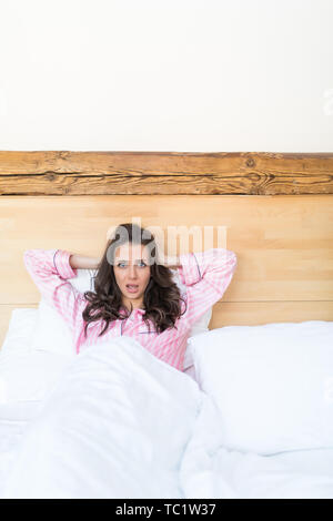 Belle journée rêveur. Vue de dessus de belle jeune femme tenant les mains derrière la tête en position couchée dans le lit Banque D'Images