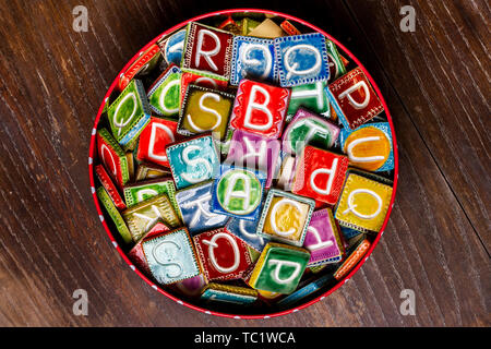 Tin Can plein de carreaux de céramique colorés avec des lettres sur la texture du bois Banque D'Images
