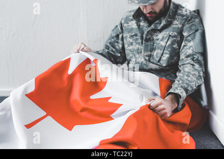 L'homme déprimé en uniforme militaire assis sur le plancher en coin et tenant le drapeau national du canada Banque D'Images