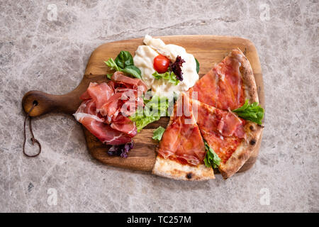 Close up of s tranches de pizza sur une planche de bois plat avec de la fumé speck jambon de Parme, fromage gorgonzola , salade fraîche sur une table de marbre gris blanc voir fr Banque D'Images