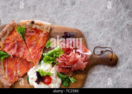 Gros plan d'une pizza en tranches sur une planche en bois plat avec de la fumé speck jambon de Parme, fromage gorgonzola , salade fraîche sur une table de marbre gris blanc voir fr Banque D'Images