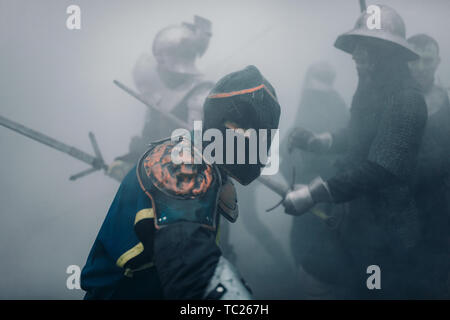 L'Escouade de combat de chevaliers médiévaux des croisés sont dans les armures et casques pendant la bataille avec des épées dans matin brumeux. Banque D'Images