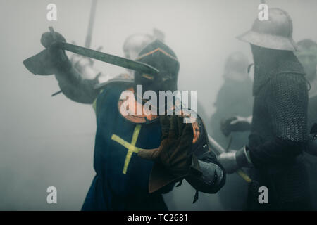 L'Escouade de combat de chevaliers médiévaux des croisés sont dans les armures et casques pendant la bataille avec des épées dans matin brumeux. Banque D'Images