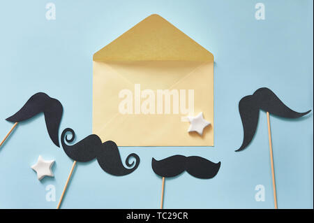 Mockup moustaches noires sur fond de papier bleu et enveloppe jaune. Carte de vœux de fête des pères avec emplacement pour le texte. Vêtements taille basse pour la pose à plat Banque D'Images