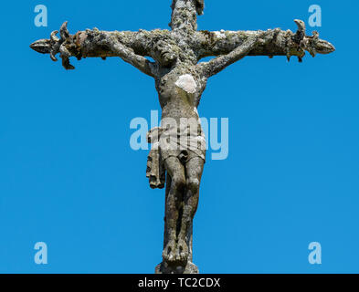 Statue de pierre du Christ sur la croix contre un ciel bleu à un cimetière de la Feuillée, Bretagne, France. Banque D'Images