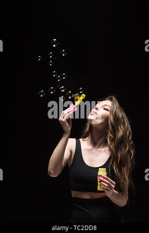 Pretty young woman blowing soap bubbles isolated on black Banque D'Images