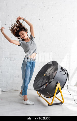 Joli happy woman in blue jeans debout avec les mains posées en face de ventilateur de soufflage Banque D'Images