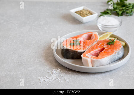 Poisson frais. darnes de saumon frais avec le citron, les épices et le sel dans une assiette. Banque D'Images