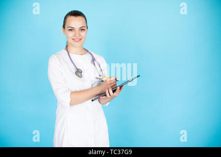 Jeune blonde female doctor with stethoscope sur son cou et comprimé sur fond bleu clair avec un espace réservé au texte Banque D'Images