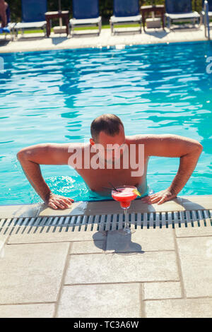 L'homme se détendre à la piscine. Une vue de face du jeune garçon appréciant les vacances en Grèce à la piscine et boire un cocktail d'alcool de fruits Banque D'Images
