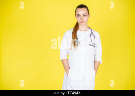 Jeune blonde female doctor with stethoscope sur son cou. Médecin à la recherche de l'appareil photo sur fond jaune avec un espace réservé au texte Banque D'Images