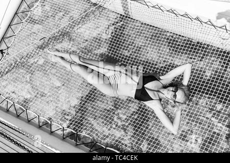 Bronzage du bikini Womanin et détente lors d'une croisière en voilier d'été, dans un hamac de catamaran de luxe. Banque D'Images