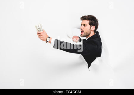 Angry businessman holding dollar billets derrière le trou du mur blanc sur papier Banque D'Images