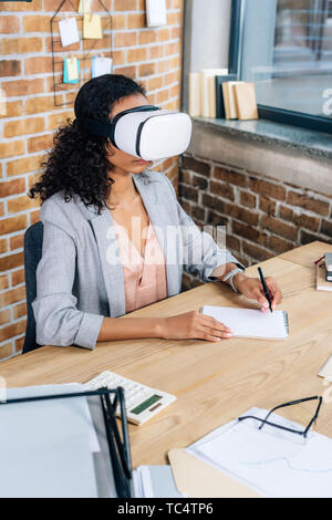 African American Casual businesswoman in casque de réalité virtuelle écrit dans l'ordinateur portable au bureau 24 Banque D'Images