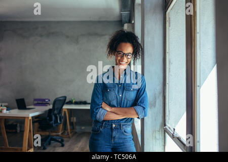 Certain entrepreneur standing in office avec les bras croisés. Smiling young businesswoman standing in office et en regardant la caméra. Banque D'Images