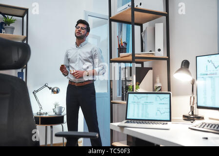 Pause cigarette. Jeune homme barbu fatigué ou commerçant dans les lunettes et l'usure formelle de fumer à son bureau moderne. Stock Exchange. Concept commercial. Concept d'entreprise. Faire une pause Banque D'Images